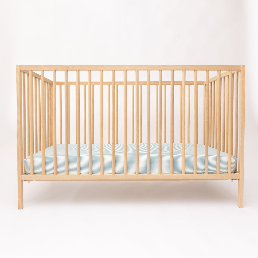 Wooden crib with a light blue mattress on a white background