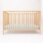 Wooden crib with a light blue mattress on a white background