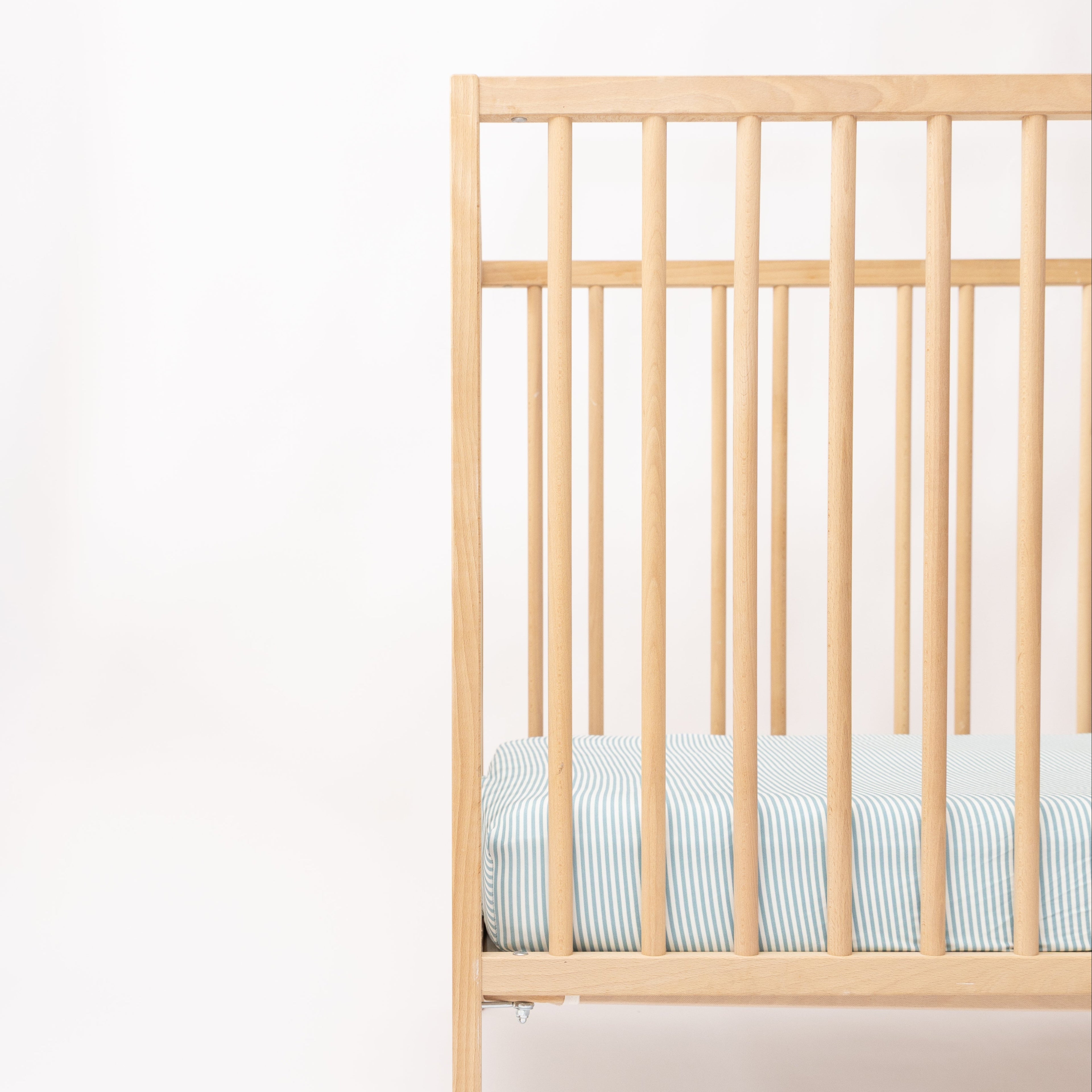 Wooden crib with a light blue mattress on a white background