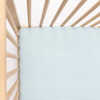 Light blue crib sheet on a wooden crib with a white background