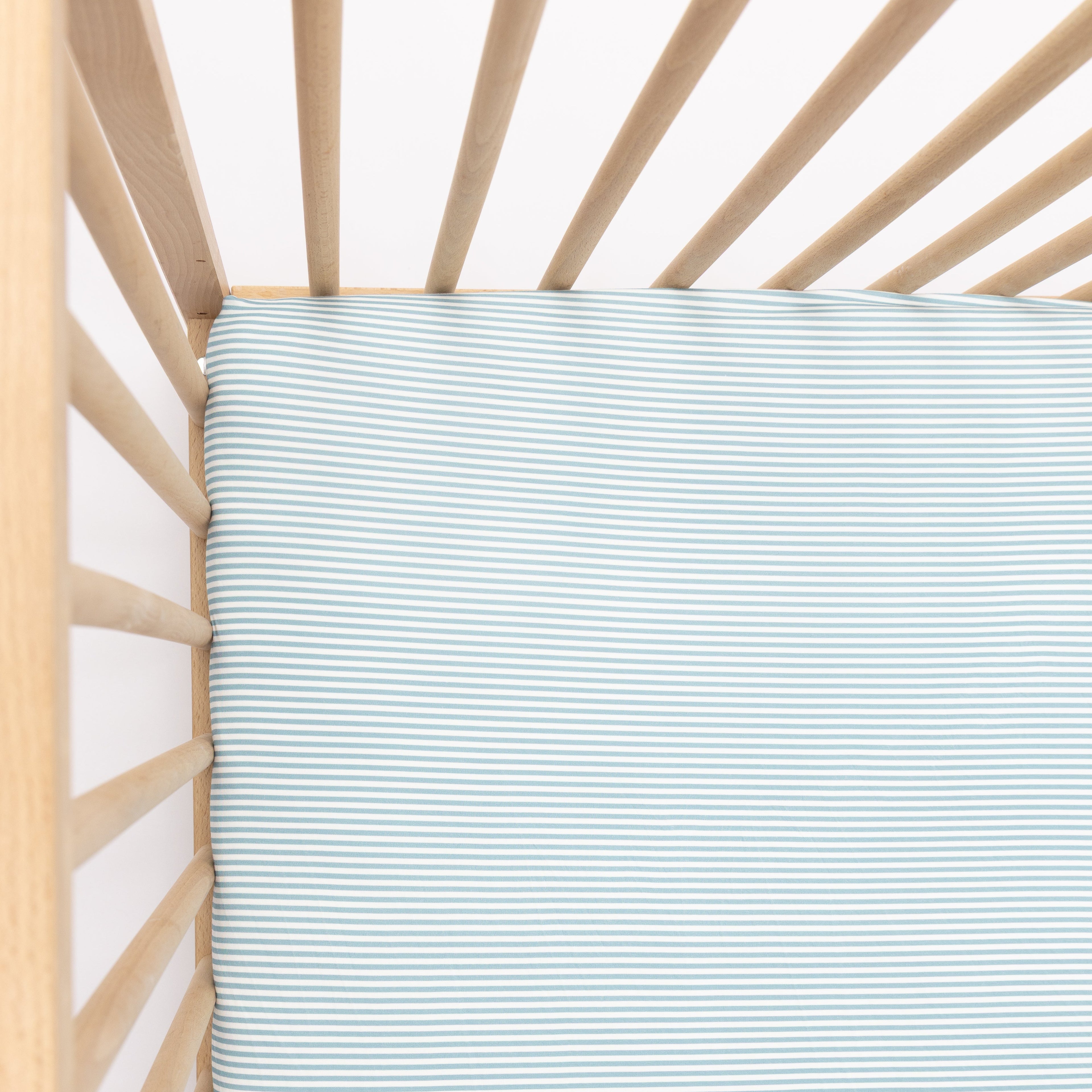 Light blue crib sheet on a wooden crib with a white background