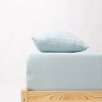 Bed with light blue striped bedding and a wooden frame on a white background