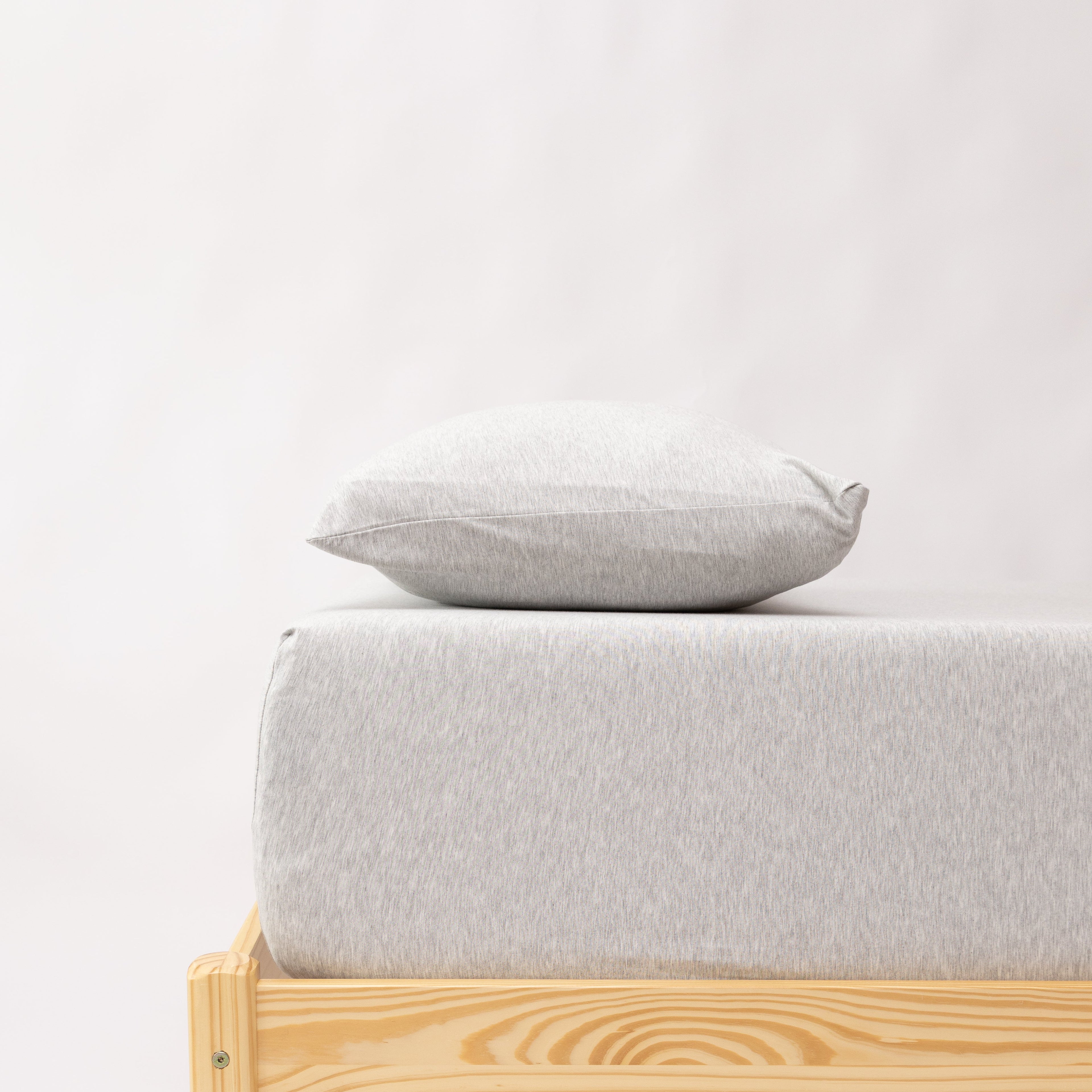 Minimalist bed with wooden frame and light gray mattress and pillow on a white background