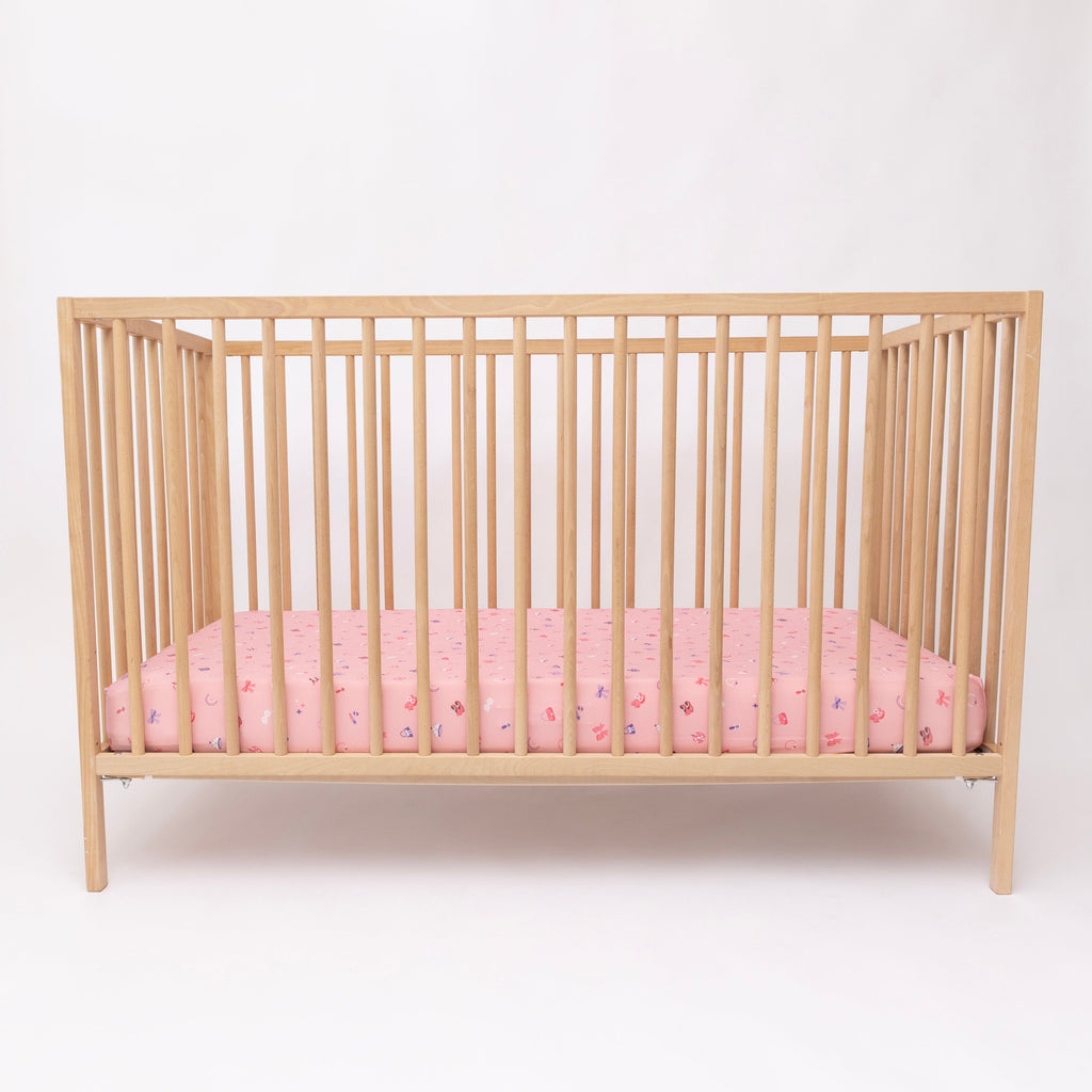 Wooden crib with pink sheets on a white background