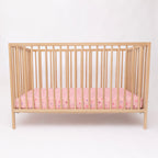 Wooden crib with pink sheets on a white background