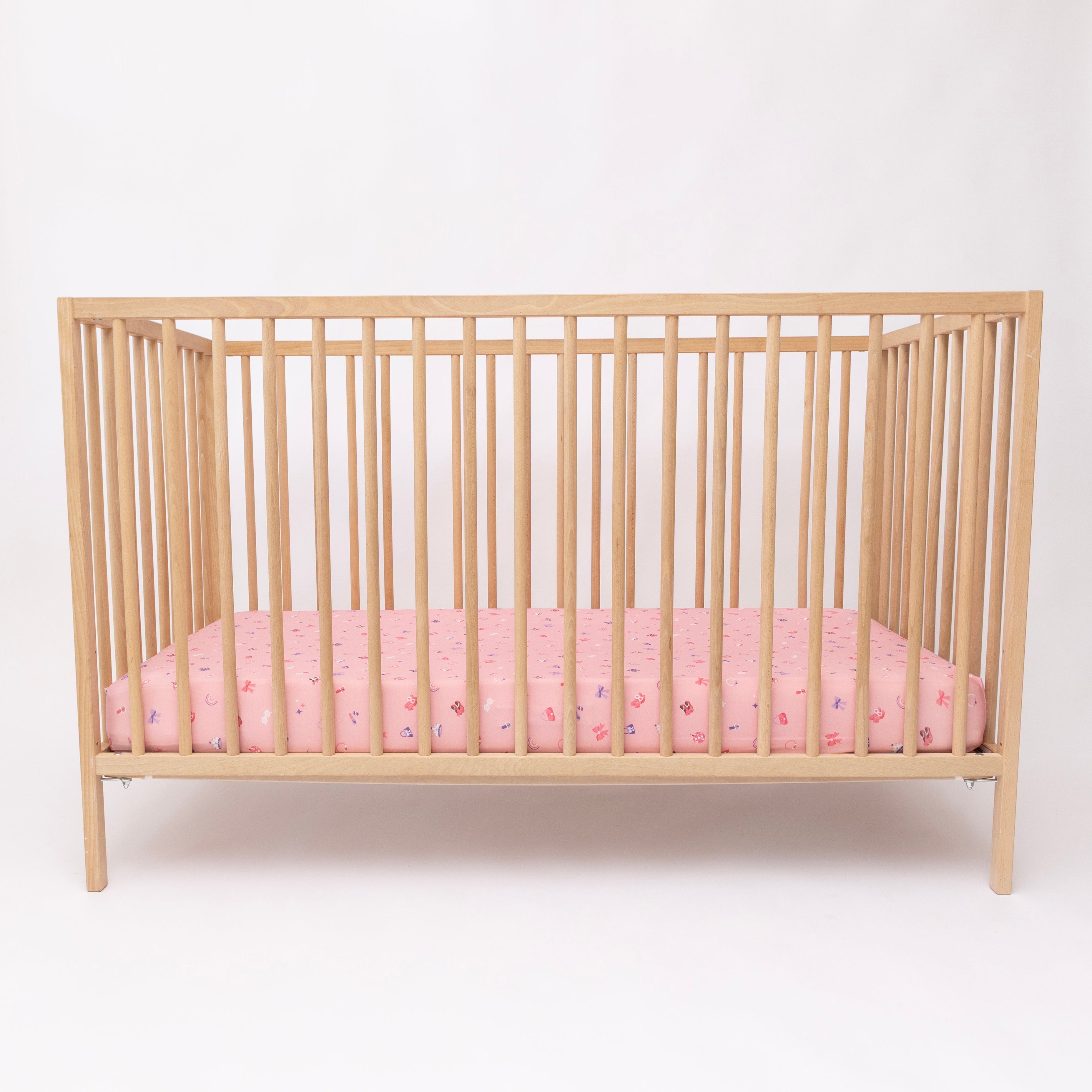 Wooden crib with pink sheets on a white background