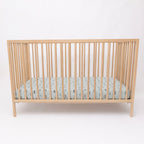 Wooden crib with a fitted sheet featuring small vehicle patterns on a light blue background