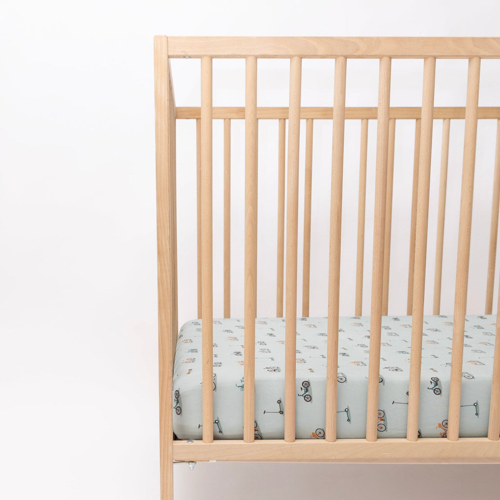 Crib with a fitted sheet featuring small vehicle patterns on a light blue background