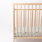 Crib with a fitted sheet featuring small vehicle patterns on a light blue background