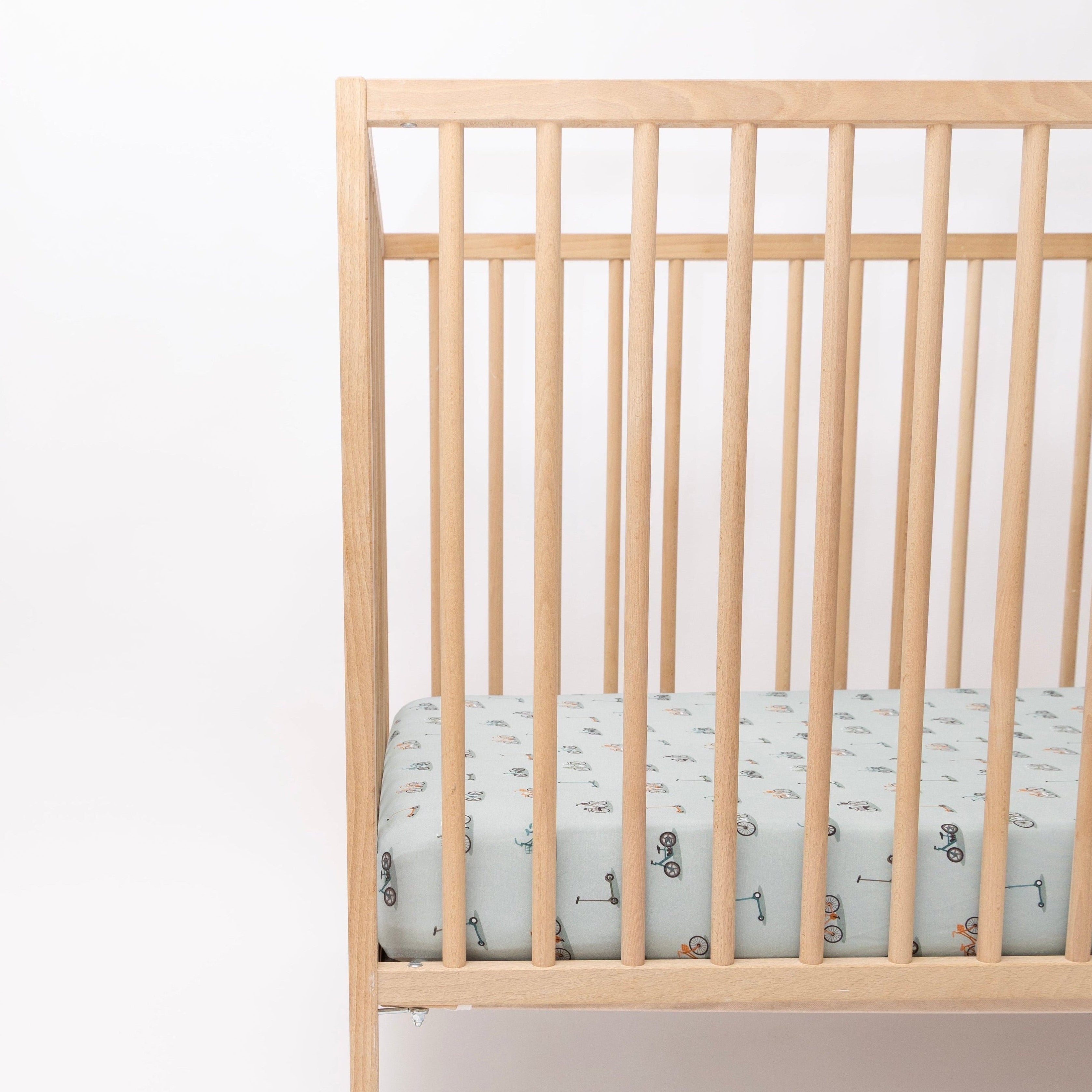 Crib with a fitted sheet featuring small vehicle patterns on a light blue background