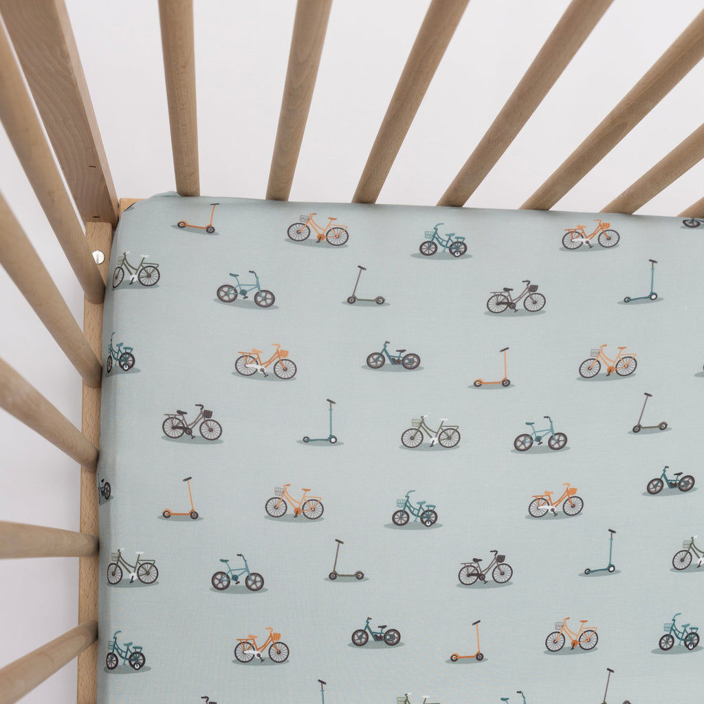 Crib with a fitted sheet featuring small vehicle patterns on a light blue background