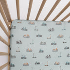 Crib with a fitted sheet featuring small vehicle patterns on a light blue background