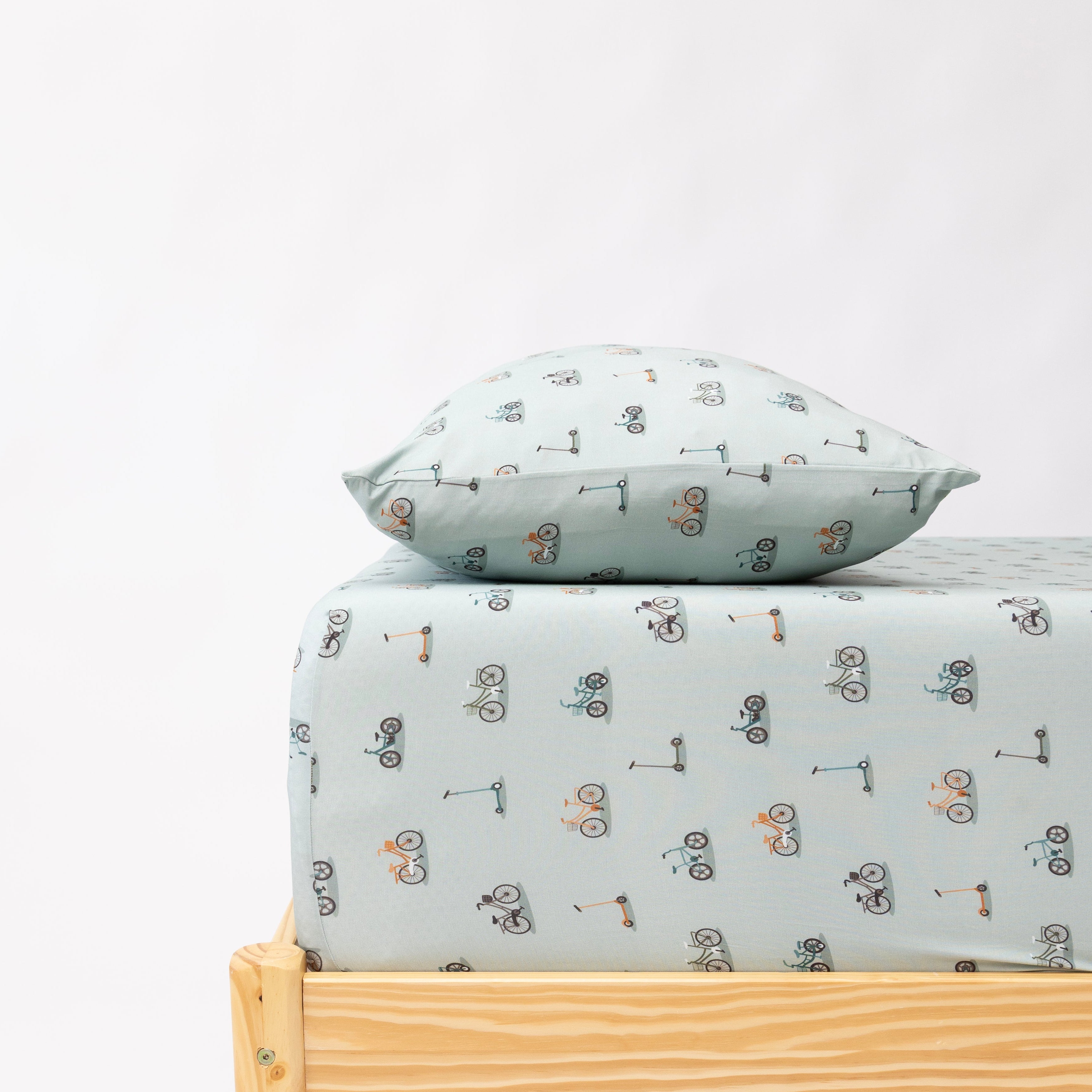 Children's bed with light blue sheet and pillow featuring bicycles & scooters on a white background