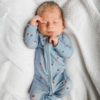 Newborn baby sleeping in a blue onesie with stars and flags on a white textured background.