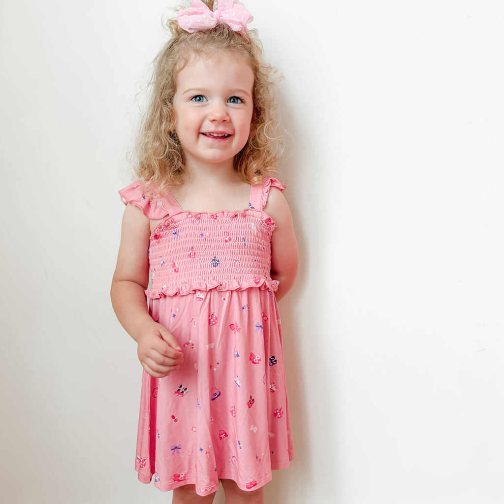 Young girl wearing a pink dress with girly patterns on a white background