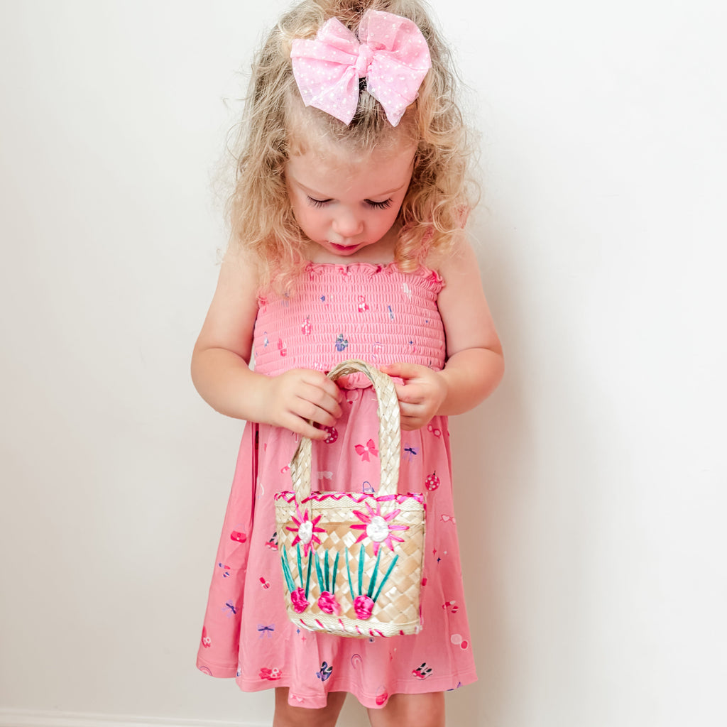 Young girl in a pink dress holding a matching bag against a plain background