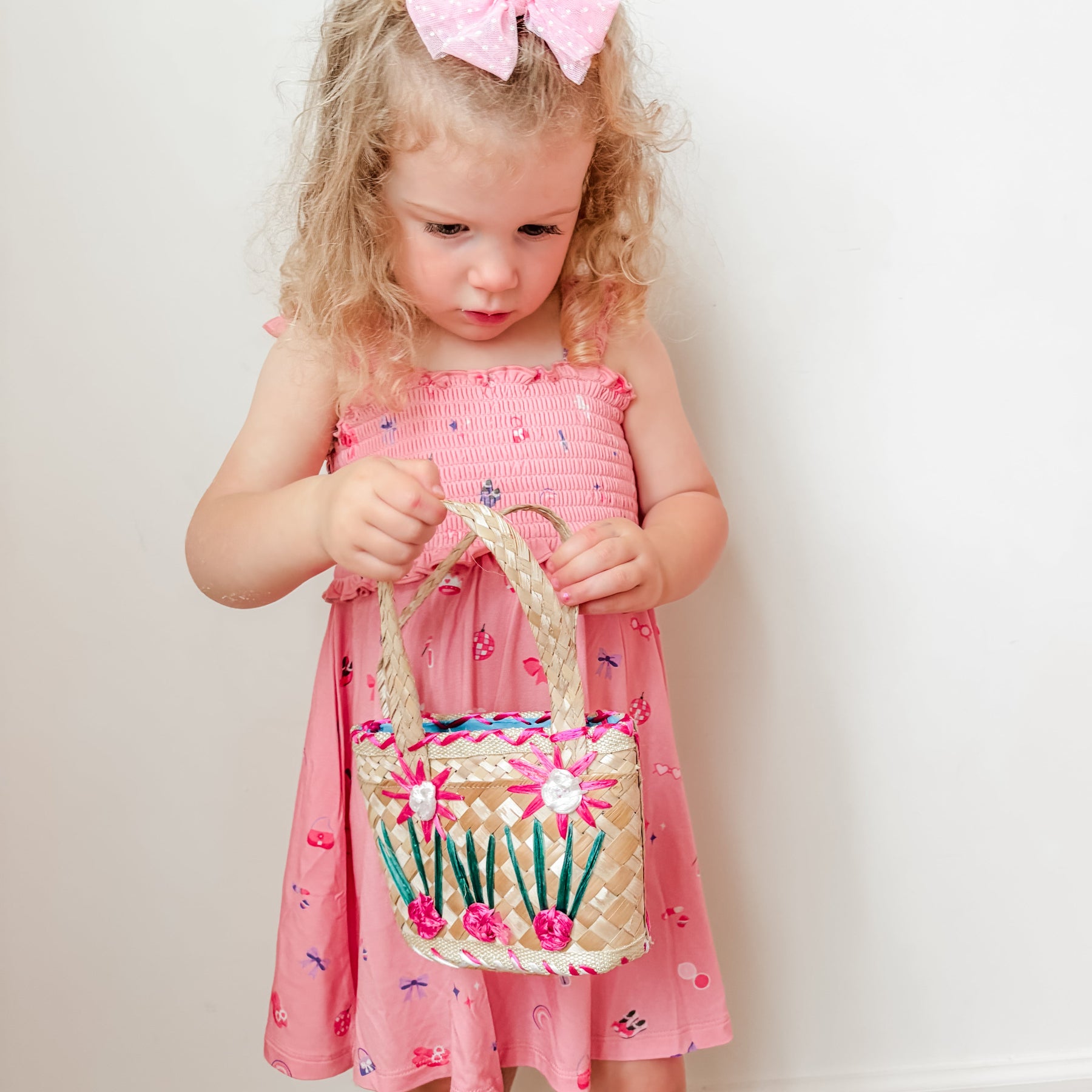 Young girl in a pink dress holding a matching bag against a plain background