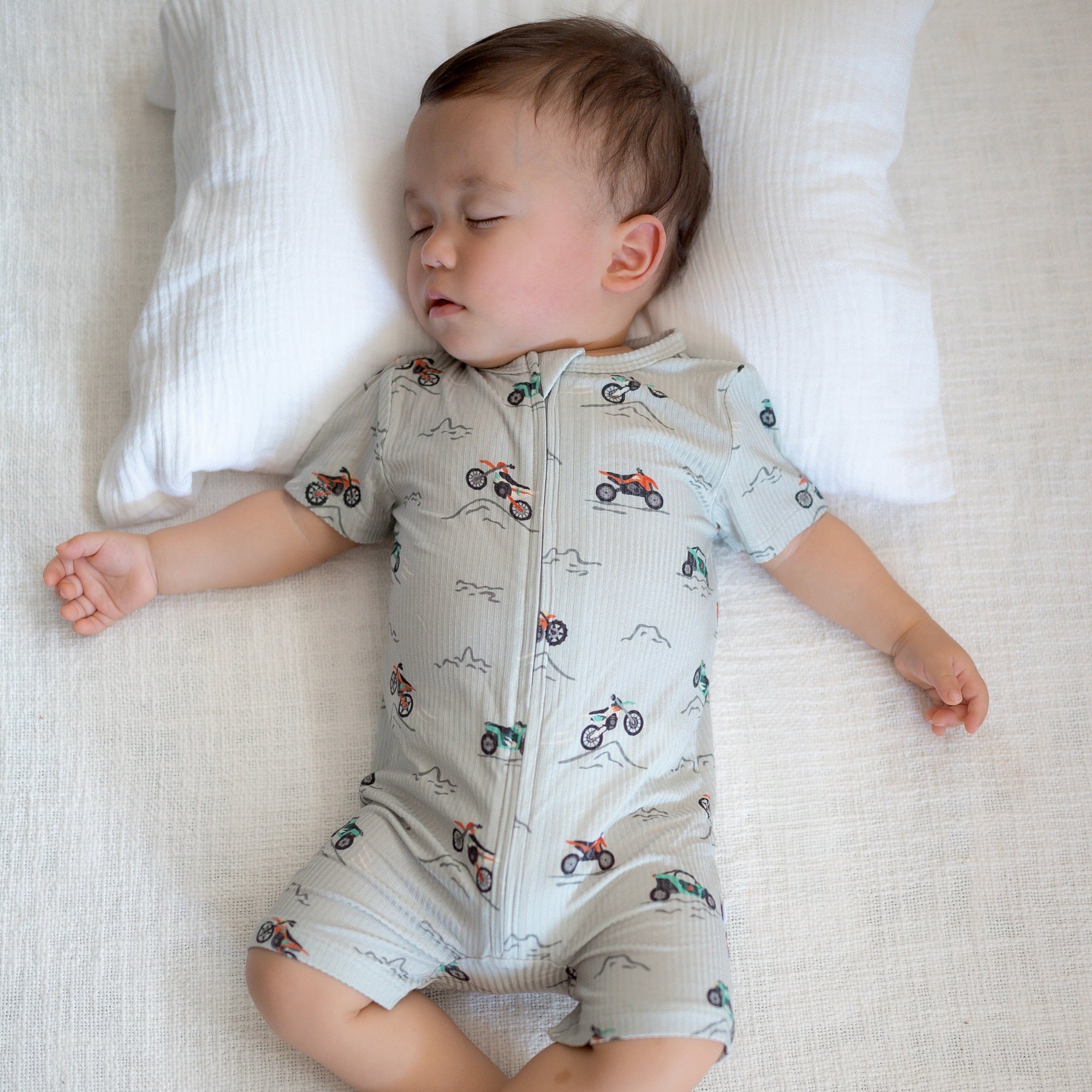 Baby wearing a light gray onesie with vehicle patterns while sleeping