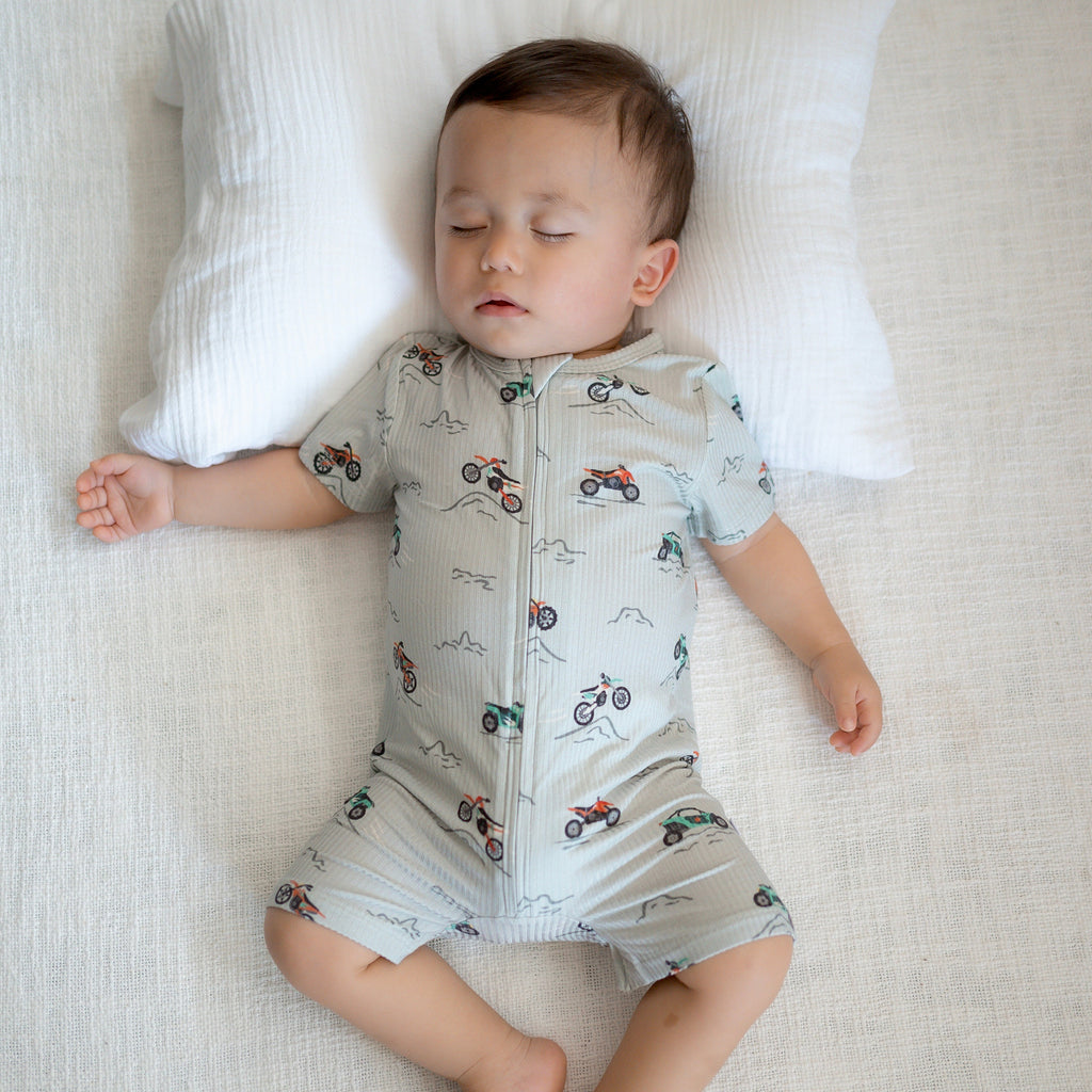 Baby wearing a light gray onesie with vehicle patterns while sleeping