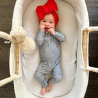Newborn baby girl wearing a blue onesie with stars and flags with red bow on a white textured background.