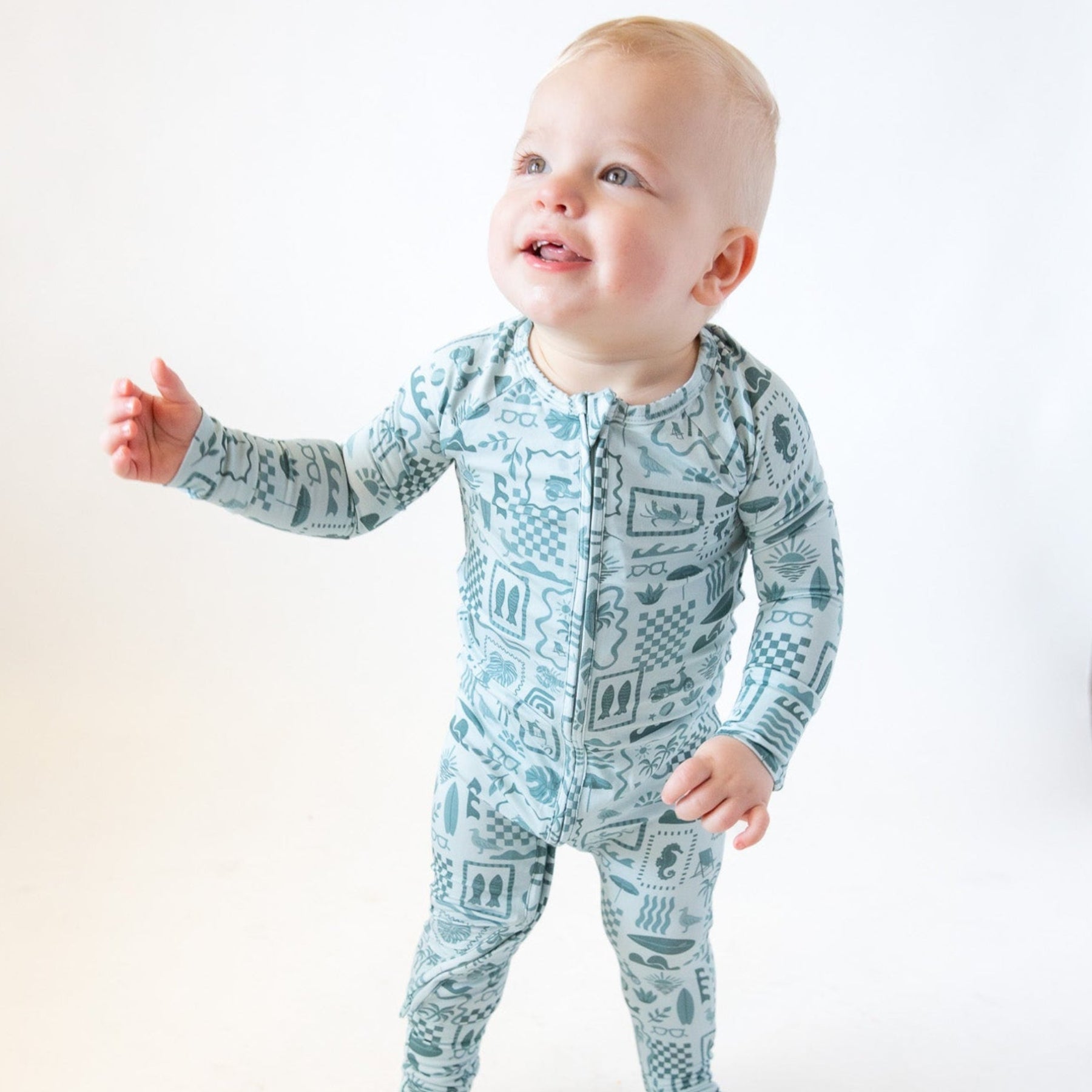 Baby wearing a blue summer-patterned onesie on a white background