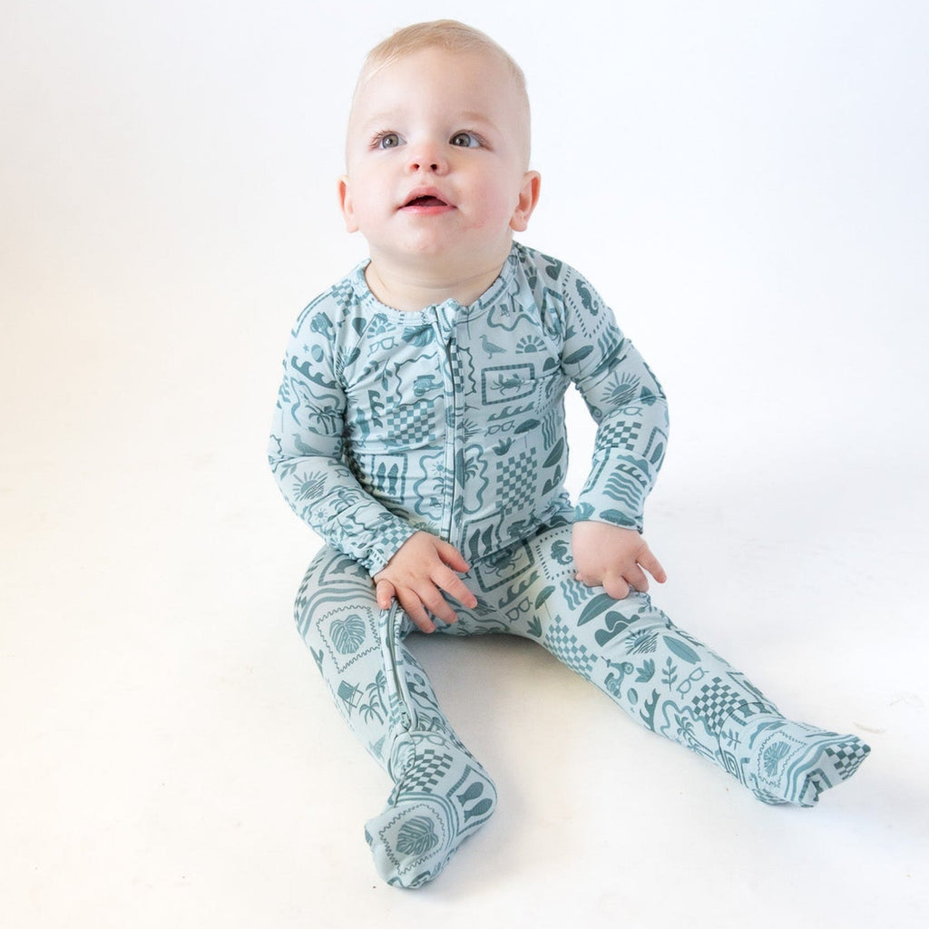 Baby wearing a blue summer-patterned onesie on a white background