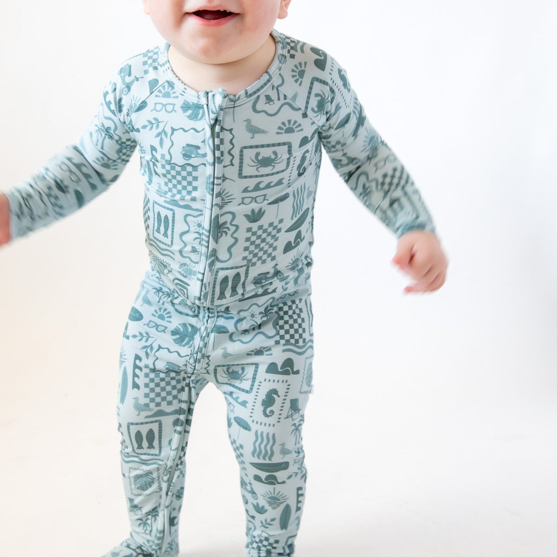 Baby wearing a blue summer-patterned onesie on a white background