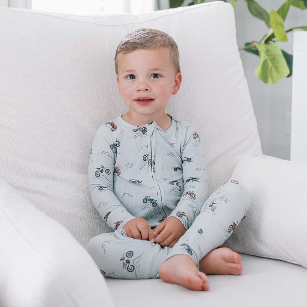 Child in light gray pajamas sitting on a white chair with a plant in the background