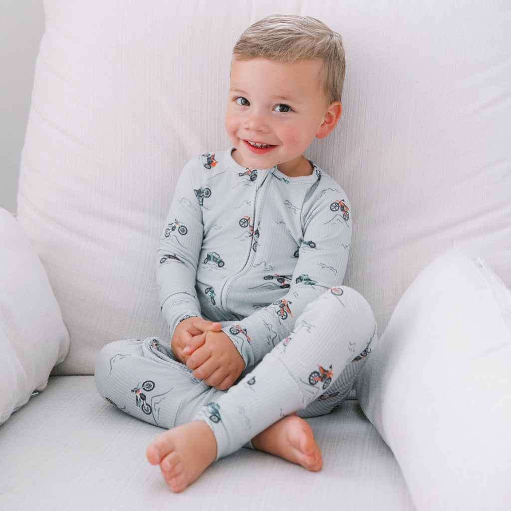 Child wearing a light gray onesie with vehicle patterns, sitting on a white chair.