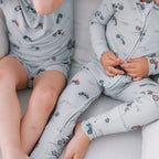 Two children wearing matching pajamas with vehicle patterns sitting on a couch.