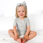 Child wearing a gray short pajamas with a matching bow on a white background