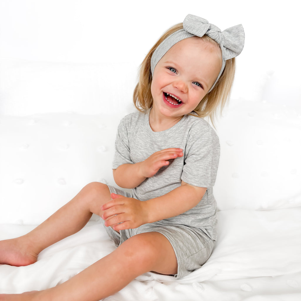 Child wearing a gray short pajamas with a matching bow on a white background