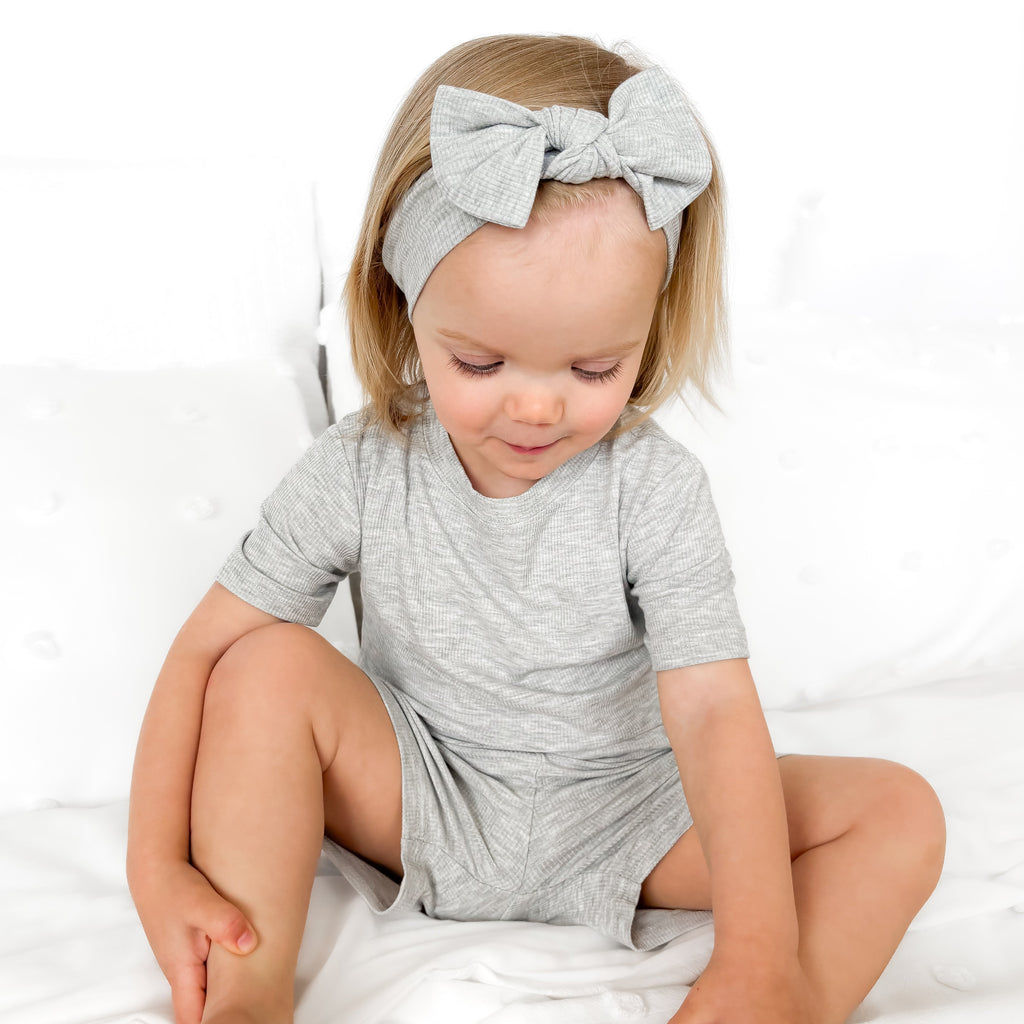 Child wearing a gray short pajamas with a matching bow on a white background