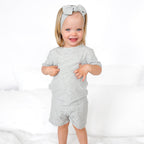 Child wearing a gray short pajamas with a matching bow on a white background