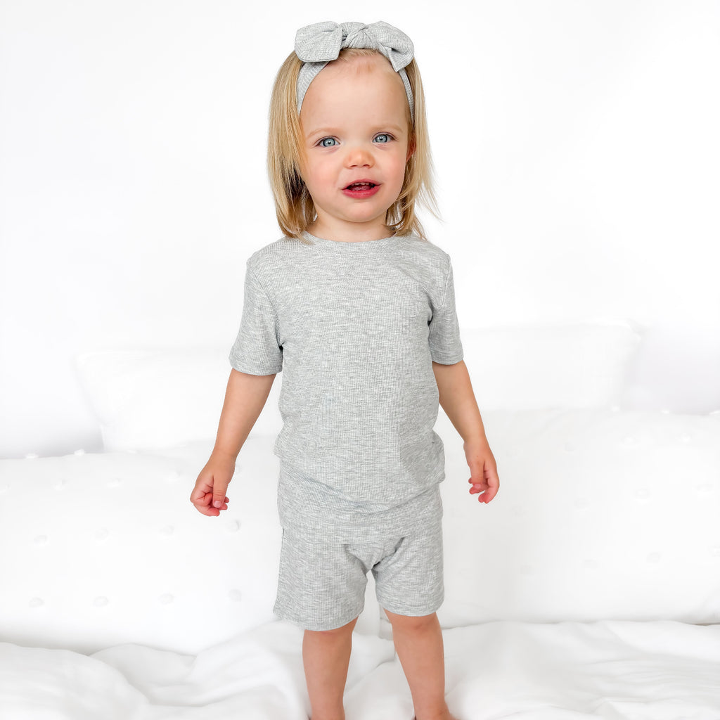 Child wearing a gray short pajamas with a matching bow on a white background