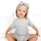 Child wearing a gray short pajamas with a matching bow on a white background