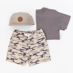 Children's outfit with camouflage shorts, gray t-shirt, and taupe cap on a white background