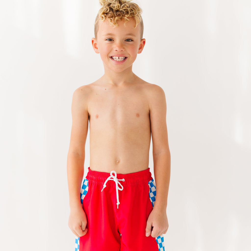Young boy wearing red swim trunks on a white background