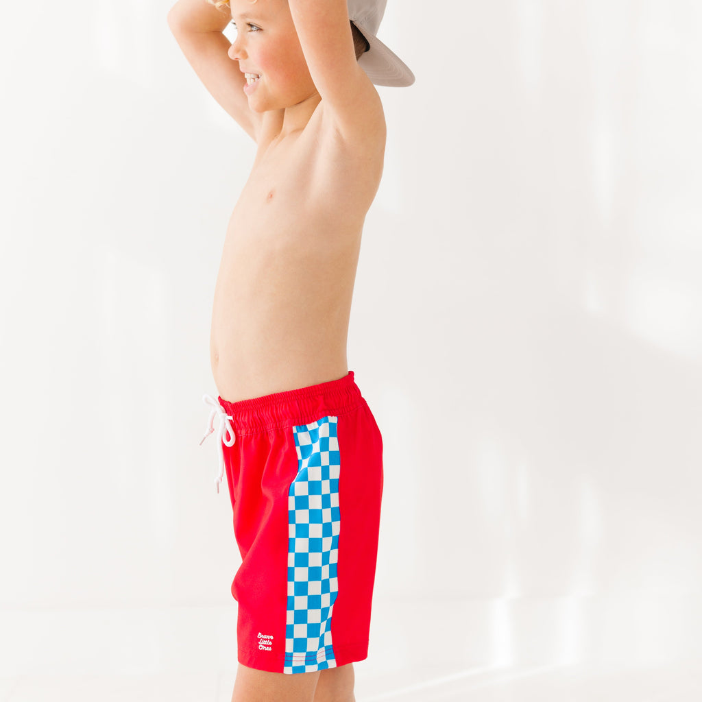 Child wearing red swim shorts with a blue and white checkered pattern on a white background