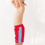 Child wearing red swim shorts with a blue and white checkered pattern on a white background
