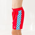 Child wearing a red swim shorts with a blue and white checkered pattern on a white background