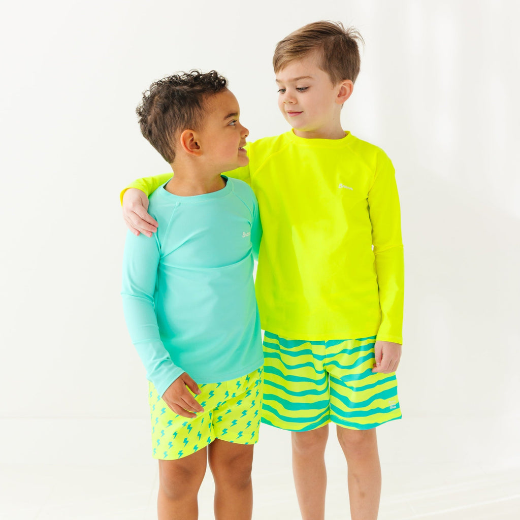 Two children wearing matching bright blue and yellow swim outfits on a white background