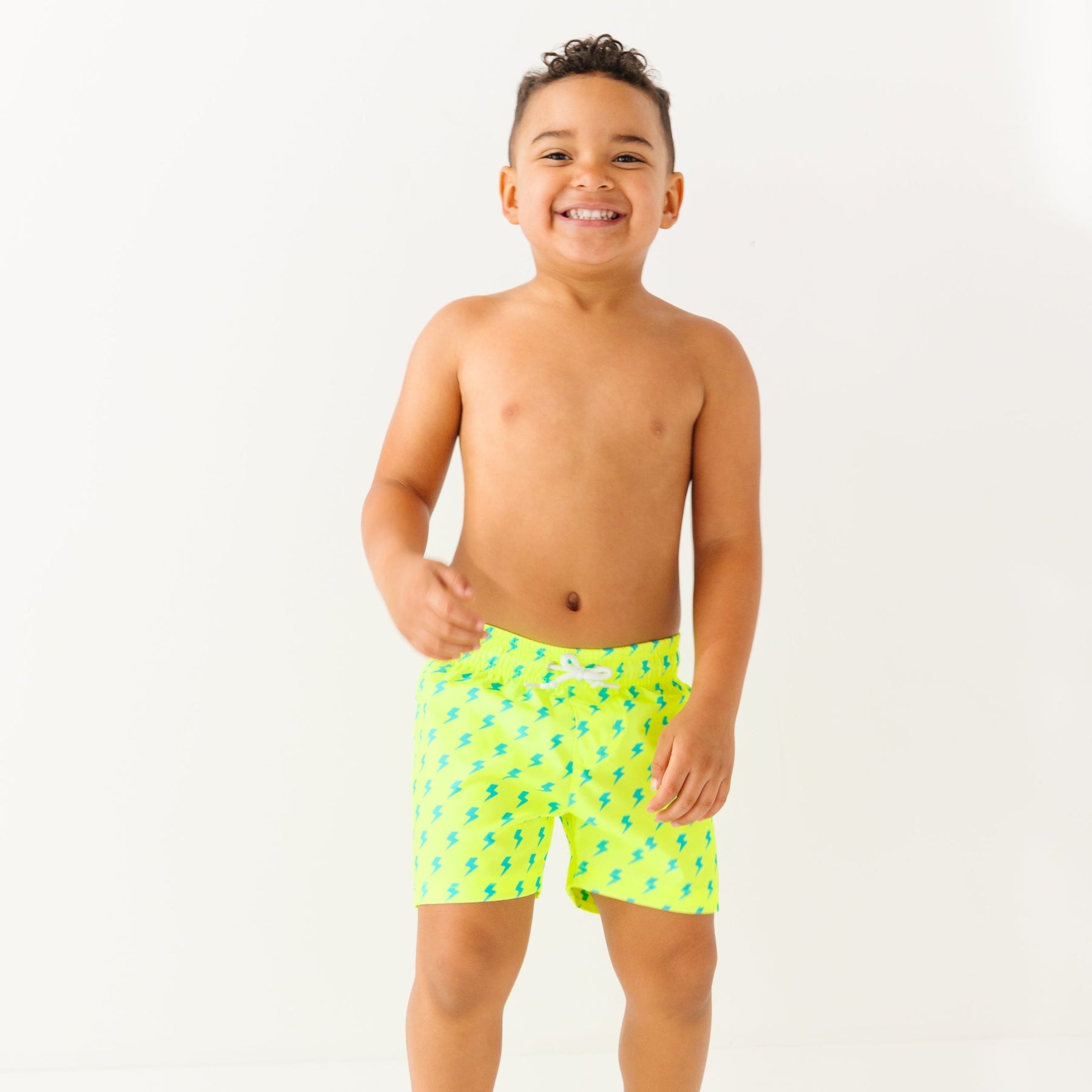 Child wearing neon yellow swim shorts with blue lightning bolt pattern on a white background