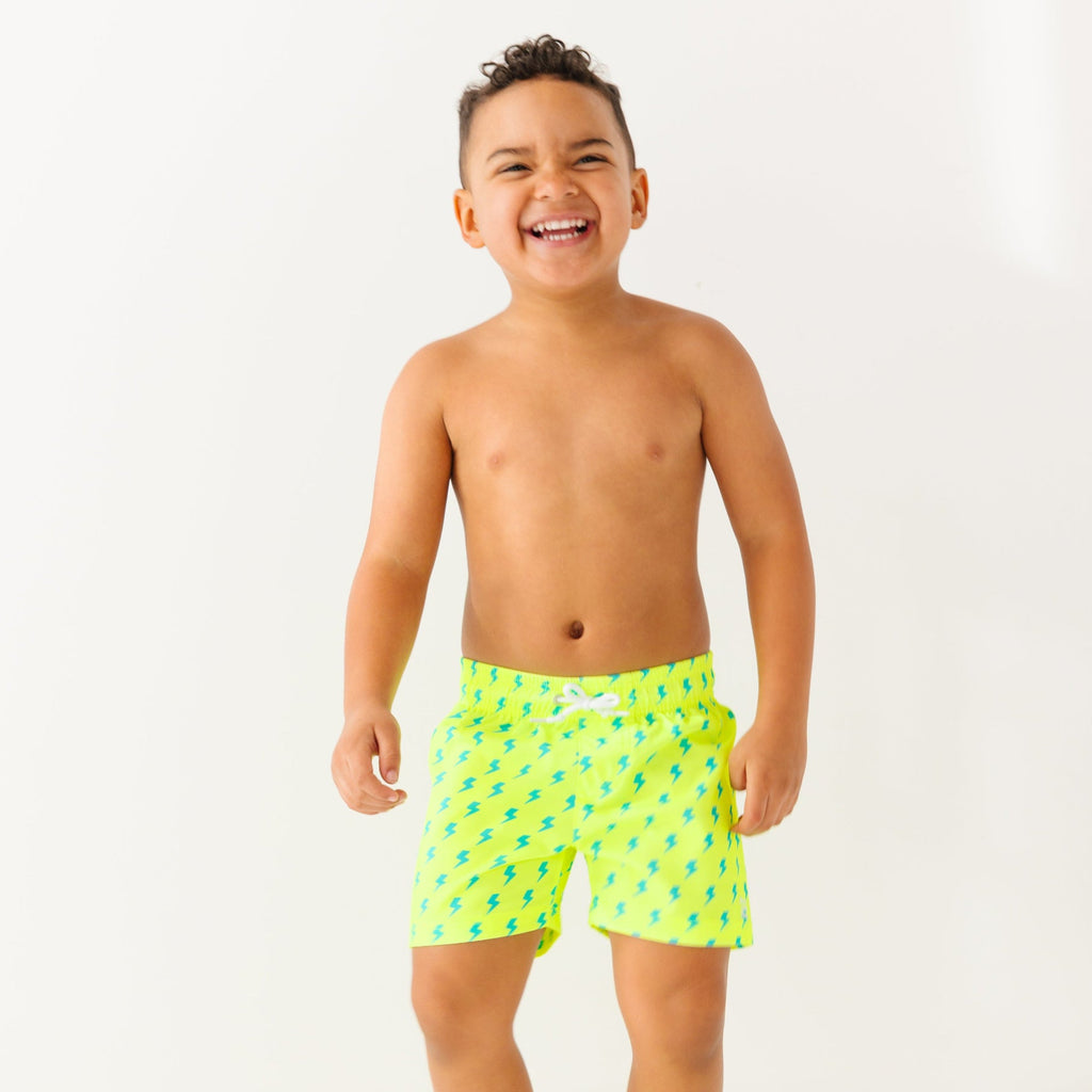 Child wearing neon yellow swim shorts with blue lightning bolt pattern on a white background