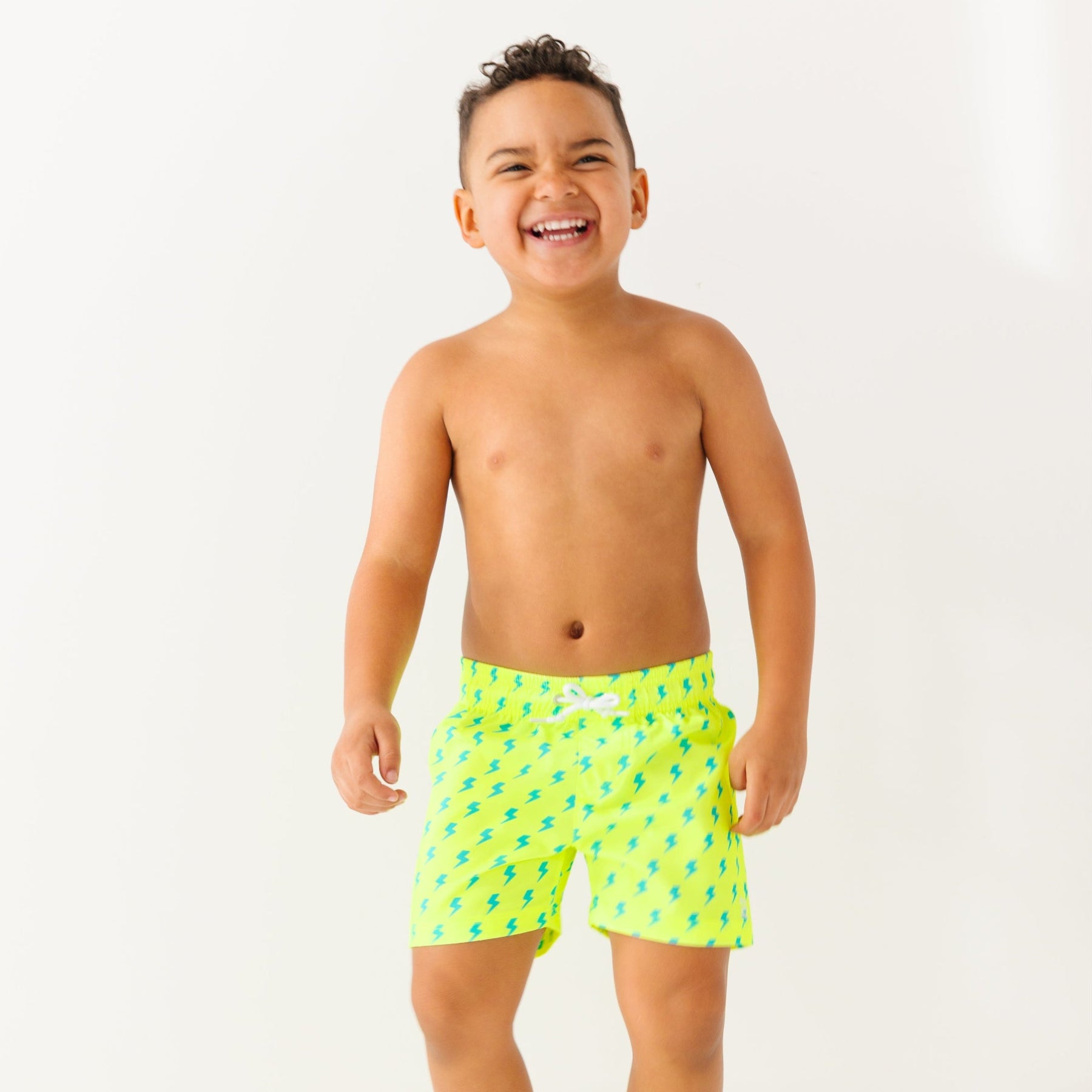 Child wearing neon yellow swim shorts with blue lightning bolt pattern on a white background