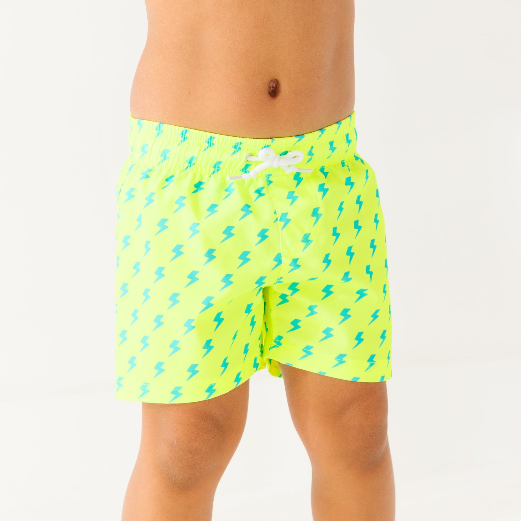Close up shot of a child wearing neon yellow swim shorts with blue lightning bolt pattern on a white background