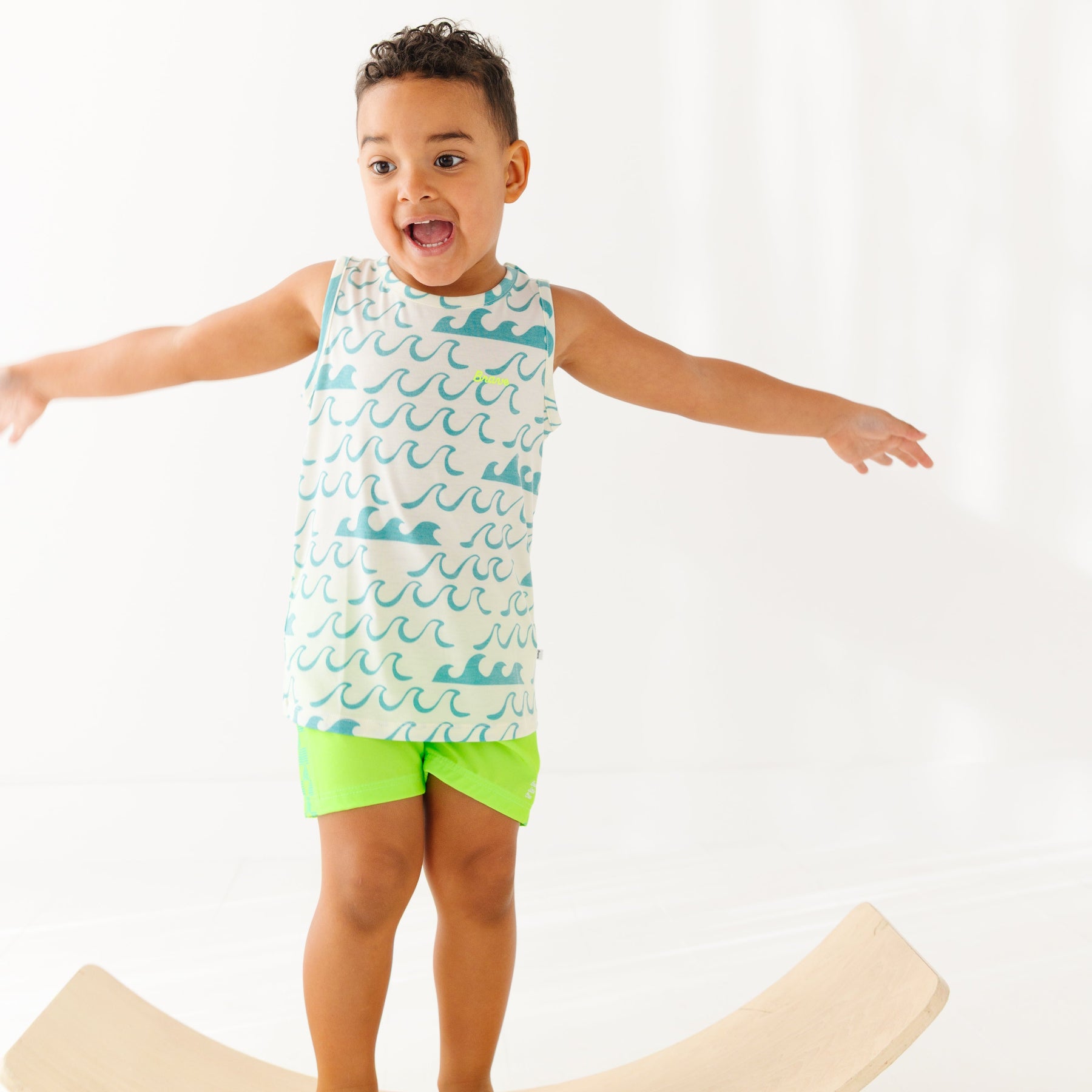 Child wearing a green checkered swim trunks and a wave-patterned top on a white background