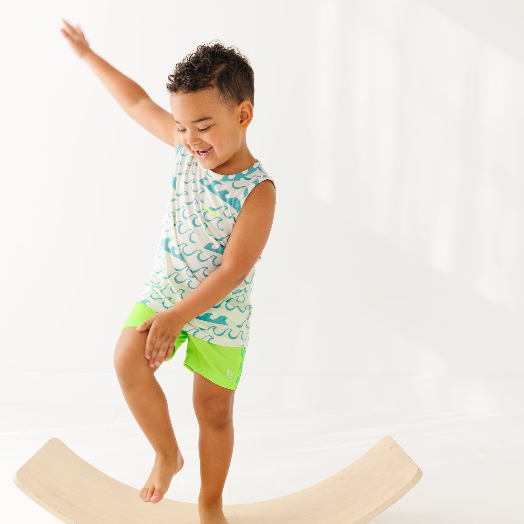 Child wearing a green checkered swim trunks and a wave-patterned top on a white background
