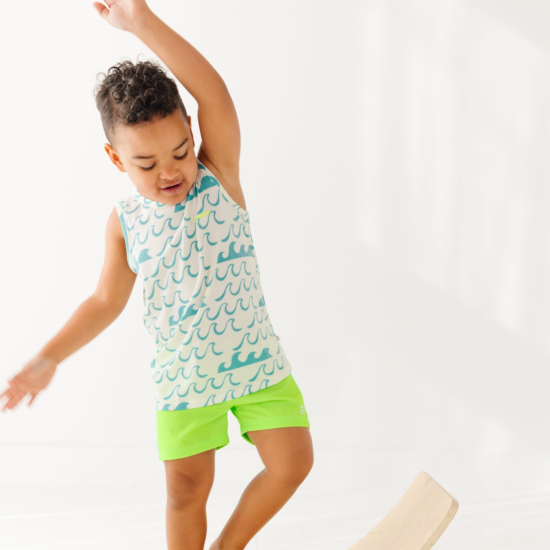 Child wearing a green checkered swim trunks and a wave-patterned top on a white background