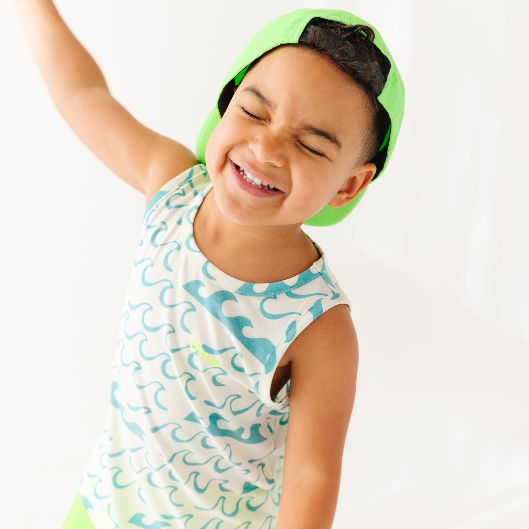 Child wearing a tank top with waves pattern and green trucker hat on a white background
